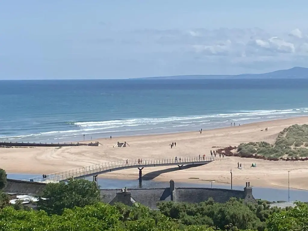 a beach with a bridge and people on the beach at J4 Lossiemouth Bay Caravan Park in Lossiemouth