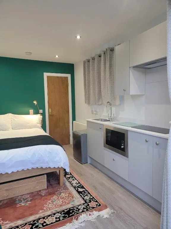 a bedroom with a bed and a kitchen with white cabinets at 'Wee Smiddy' Shepherd's Hut - Sauna - Yoga - Wild Swim in Skye of Curr