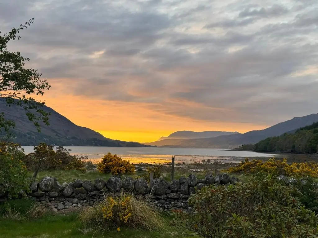 a sunset over a lake with a stone wall at Lochend Pods - Cl\u00ec Pod in Inverlael