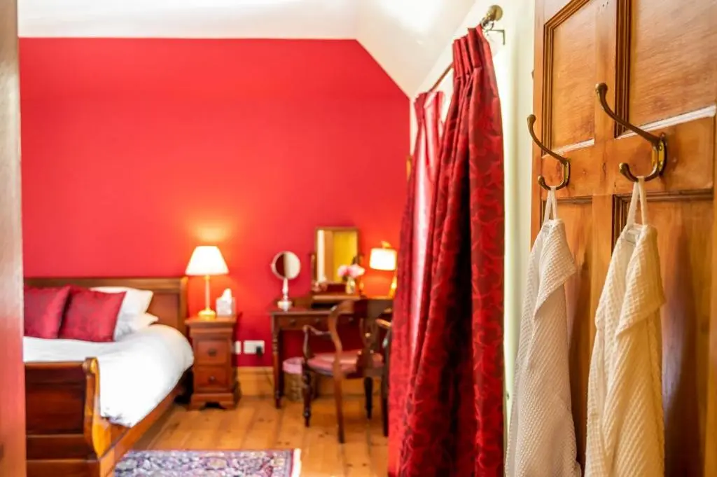 a bedroom with a red wall with a bed and a desk at Ross-shire Hall in Evanton