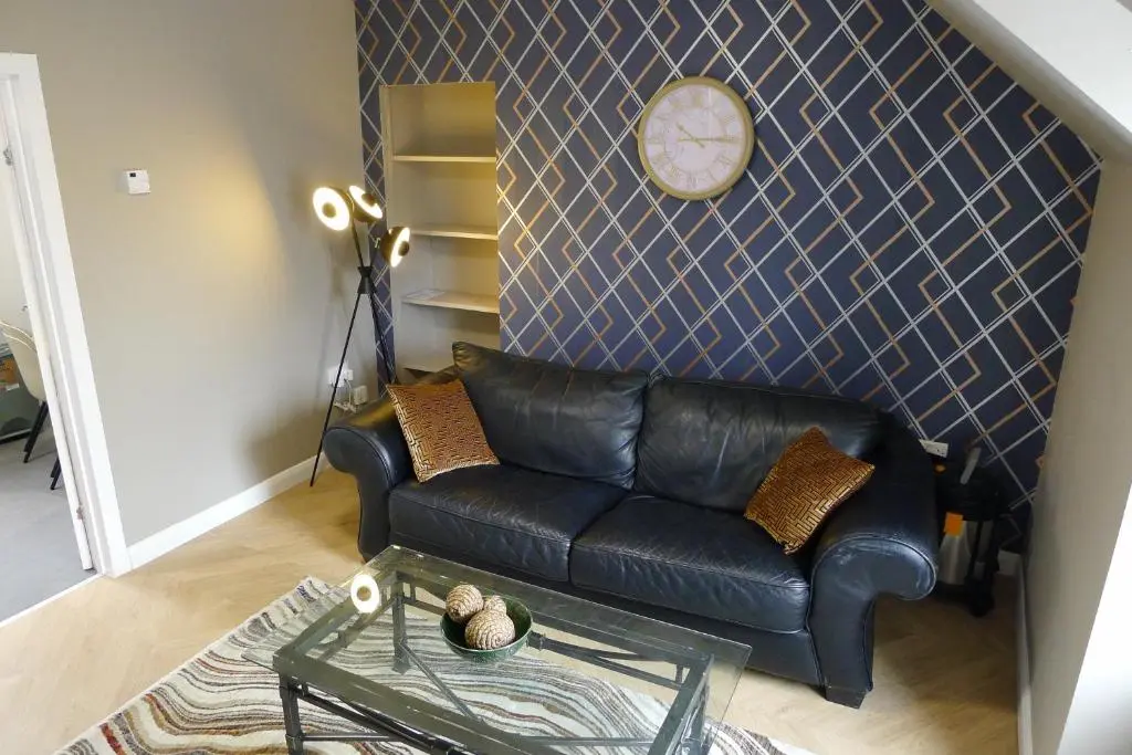 a living room with a black leather couch and a clock at Hanover st partment in Fraserburgh
