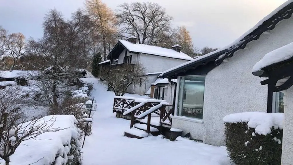 a snow covered yard with a house and a bench at Dhivach Lodge in Drumnadrochit