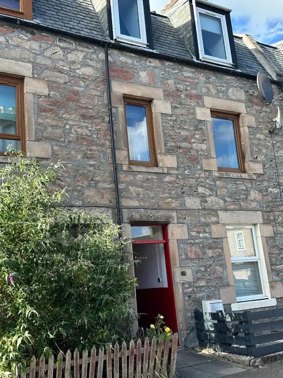 a stone house with a red door and a fence at Highland Home on the Hill in Inverness