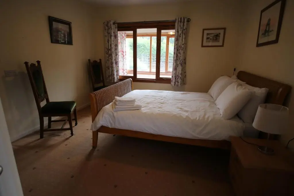 a bedroom with a bed and a window and a chair at Woodlands Rest in Garve