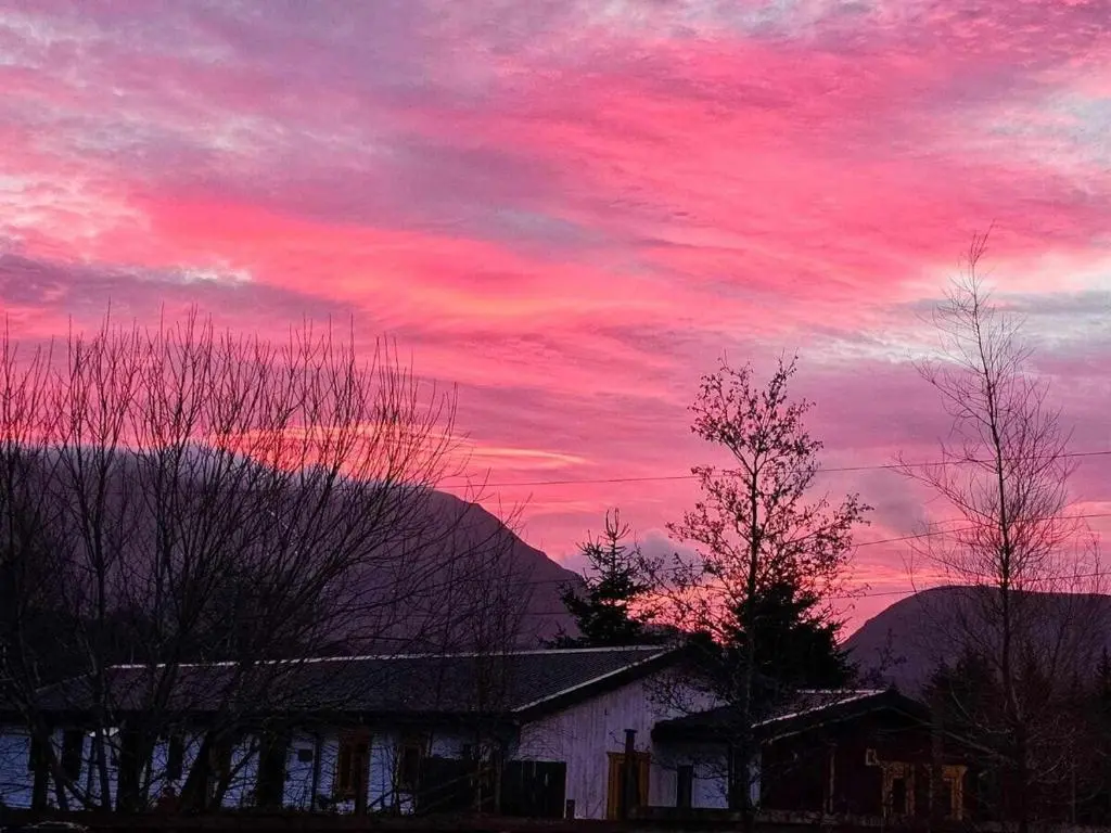 a pink sky with a house and trees in the foreground at Woodlands Rest in Garve