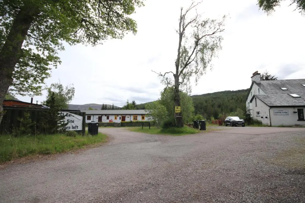 a road with two white buildings and a car on the road at Woodlands Rest in Garve