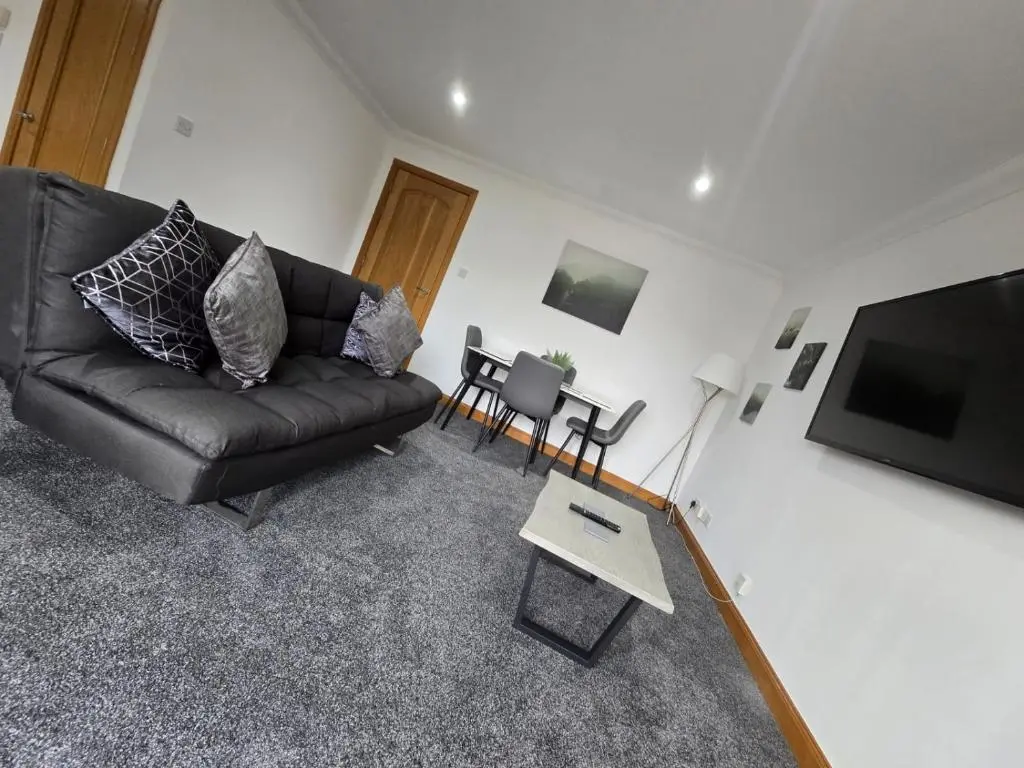 a living room with a black couch and a flat screen tv at Forres Nights in Forres