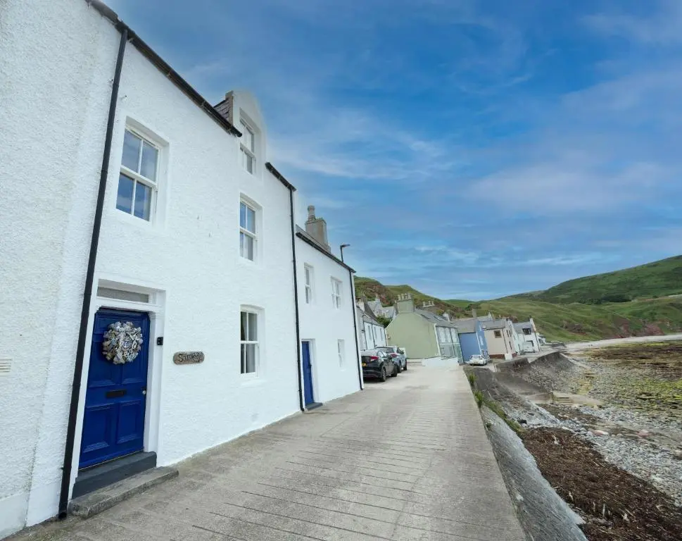a white house with a blue door on a street at Soundwaves, Seatown, Gardenstown in Gardenstown