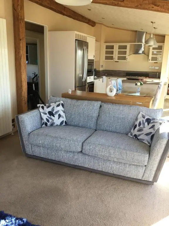 a couch in a living room with a kitchen at Rivendale Lodge in Burghead