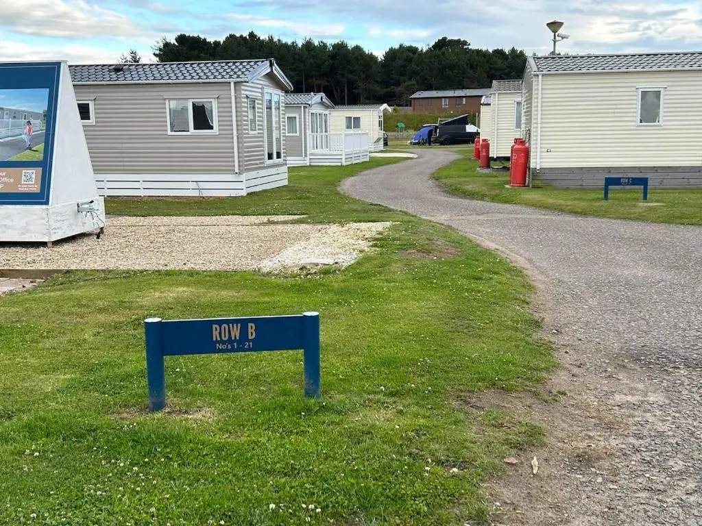 a sign in the grass next to some mobile homes at Rivendale Lodge in Burghead