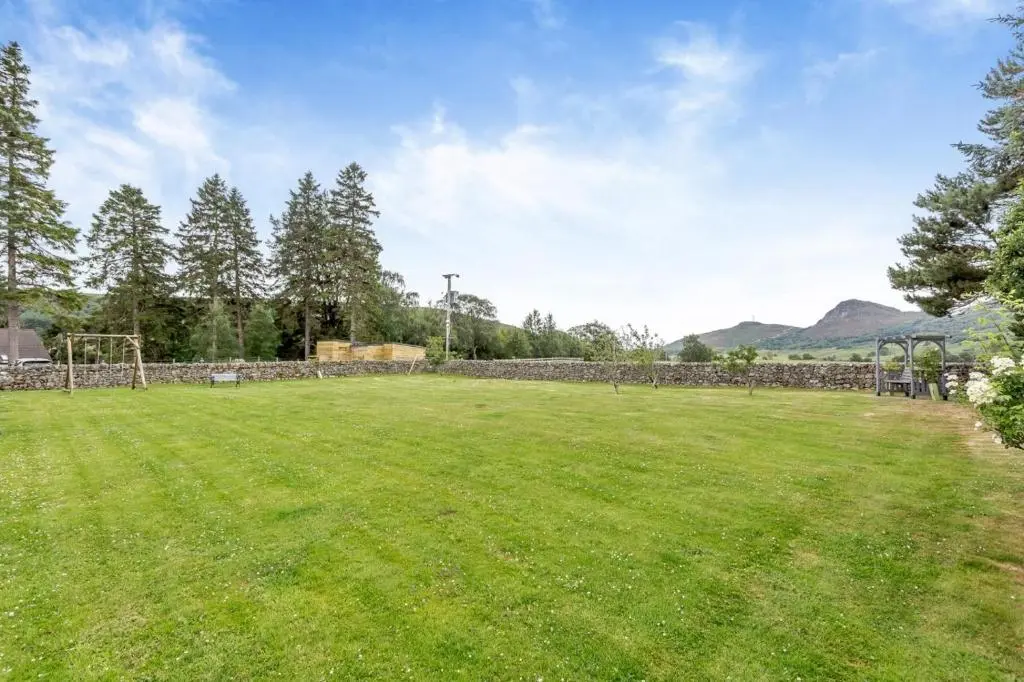 a large grassy field with a stone wall at 1 Bed in Newtonmore oc-a32412 in Newtonmore