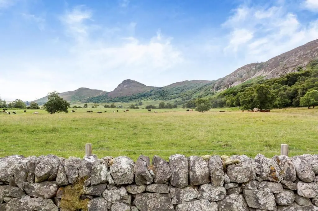 a stone wall with a field and mountains in the background at 1 Bed in Newtonmore oc-a32412 in Newtonmore