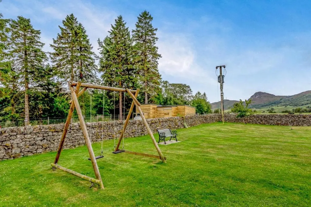 a swing set in a yard with a stone wall at 2 Bed in Newtonmore oc-d32413 in Newtonmore