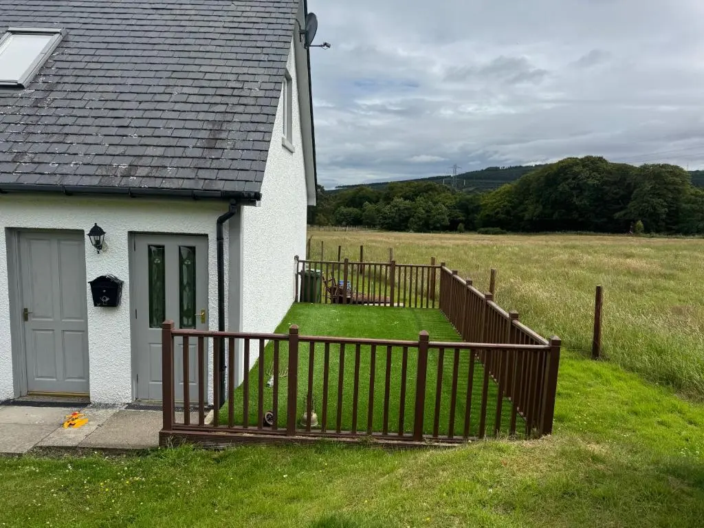 a house with a wooden fence next to a field at Daviot Lodge apartment in Daviot