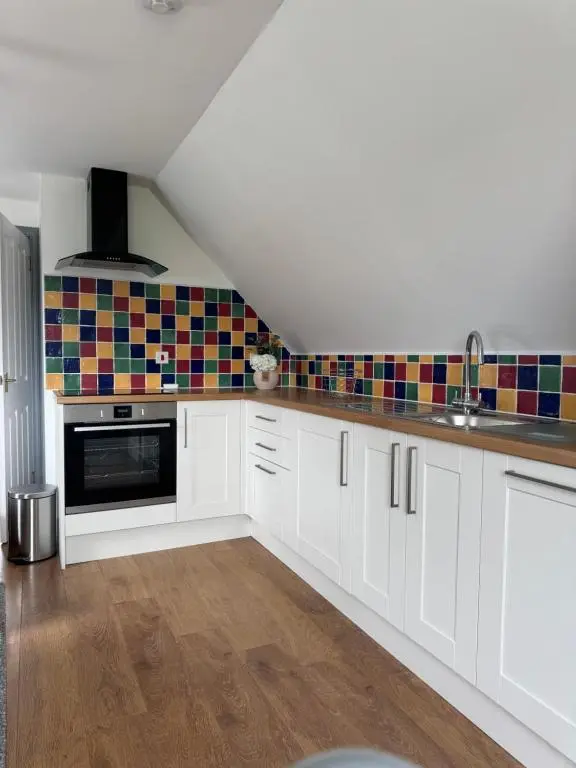 a kitchen with white cabinets and colorful tiles on the wall at Daviot Lodge apartment in Daviot