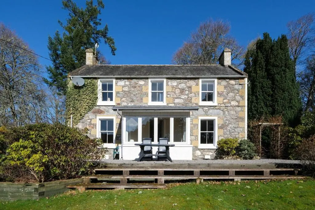 an old stone house with a bench in front of it at Gledfield Estate Holiday Cottages in Lower Gledfield