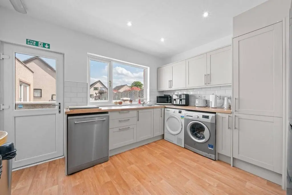 a kitchen with white cabinets and a washer and dryer at Cloudhowe Cottage Ensuite Rooms & Studio Inverness in Inverness