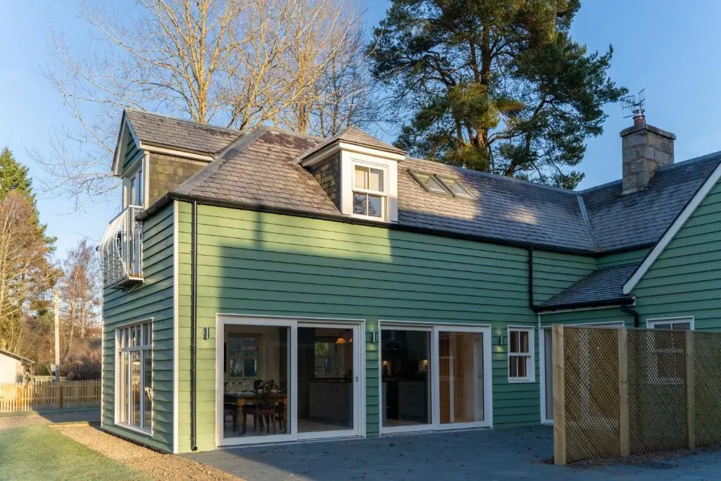 a green house with white windows and a roof at Old Coach House in Braemar