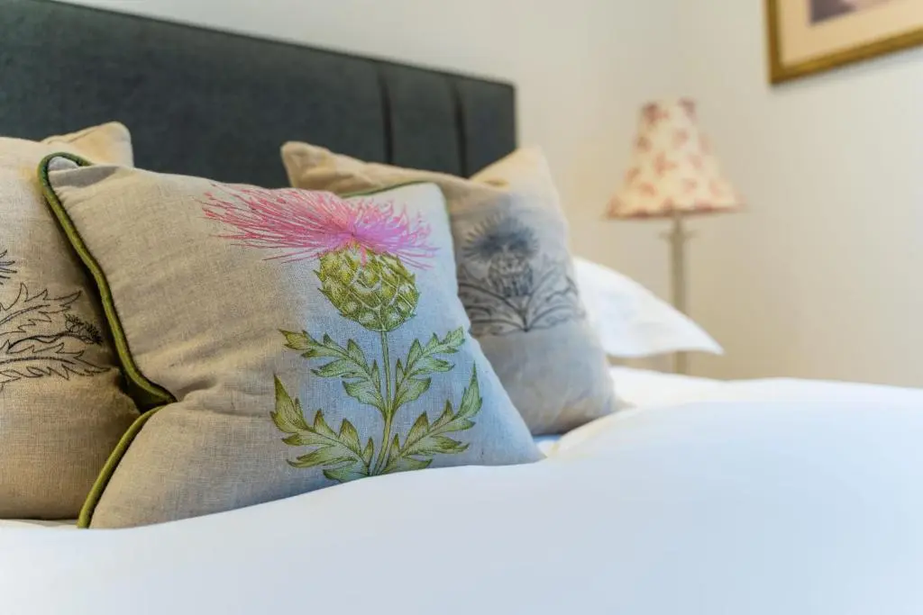 a bed with pillows with a pink flower on it at Old Coach House in Braemar