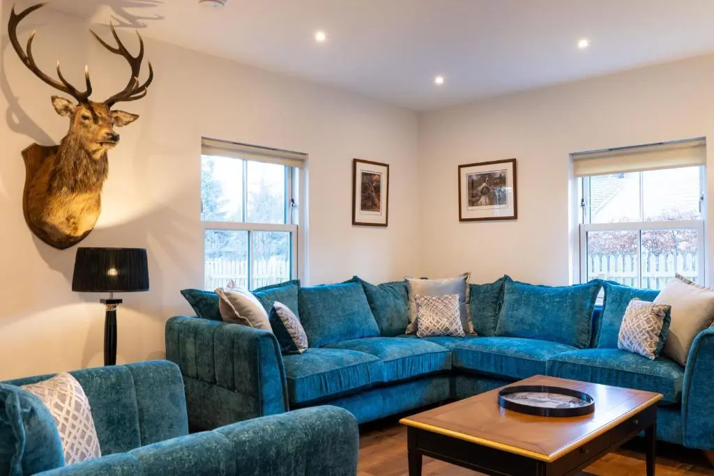 a living room with a blue couch and a deer head on the wall at The Old Coach House & The Hayloft in Braemar
