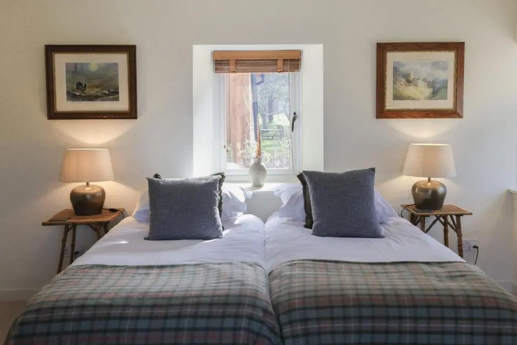two beds in a room with two lamps and a window at Relugas Mill in Forres
