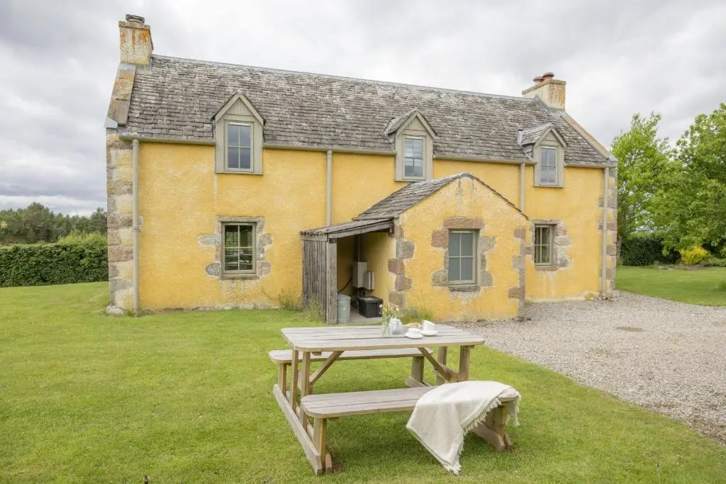 a yellow house with a picnic table in front of it at Drum Cottage in Nethy Bridge