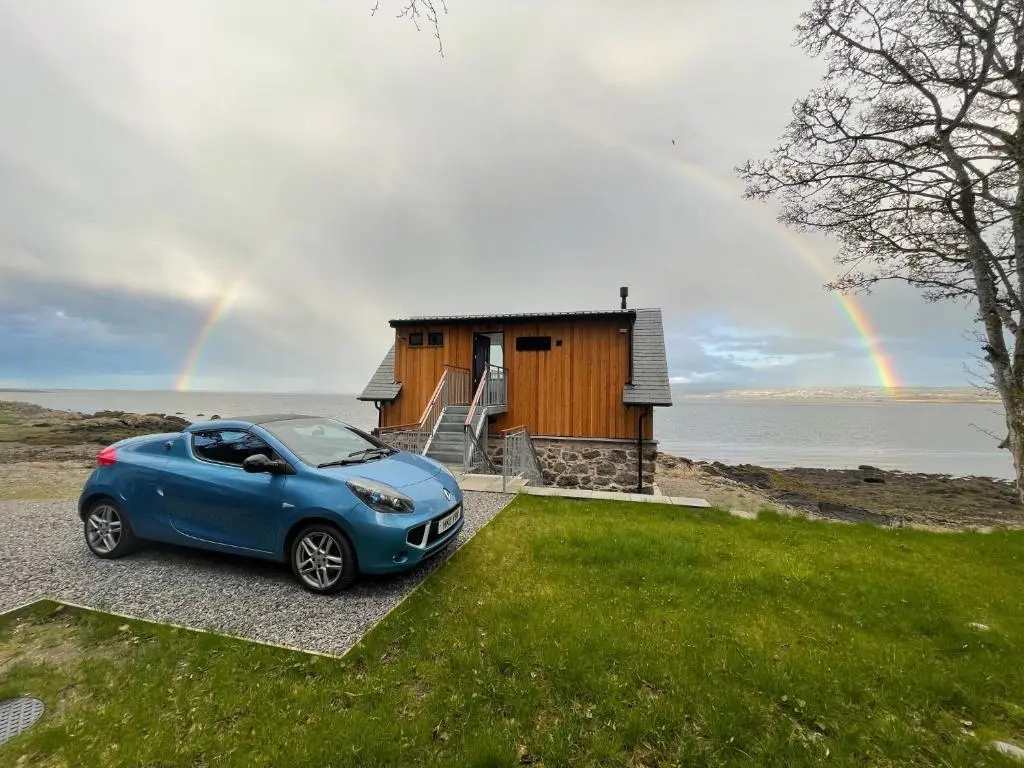 a blue car parked in front of a house with a rainbow at The Boathouse at Croft Downie in Archiestown