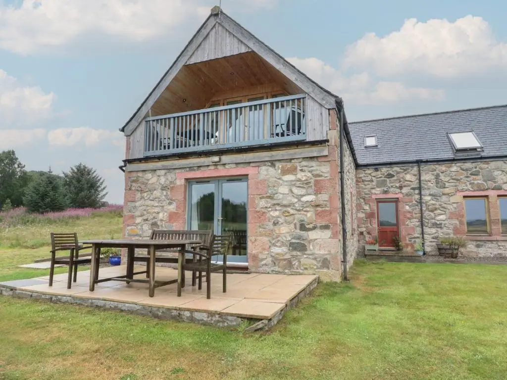 a stone cottage with a table and chairs and a balcony at Taffs Barn in Fortrose