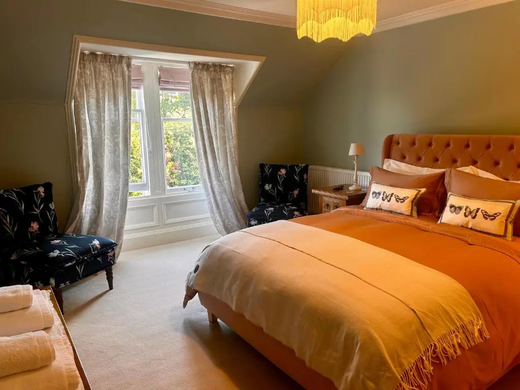 a bedroom with an orange bed and two chairs at Clashmore House in Dornoch