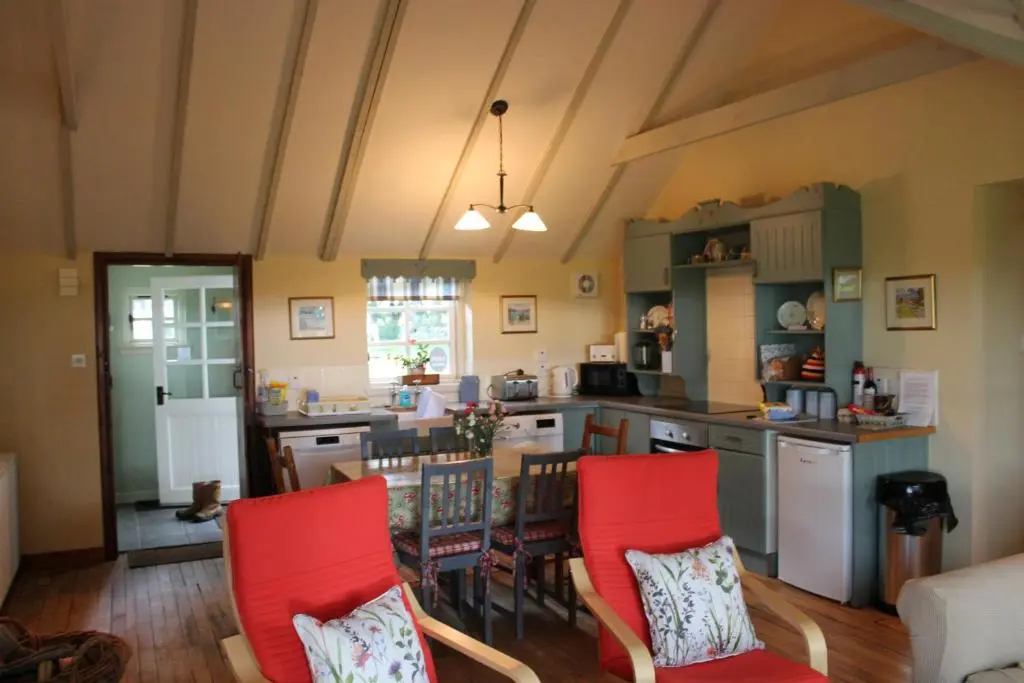 a kitchen and dining room with red chairs and a table at St Brandon House Country Cottages in Boyndie