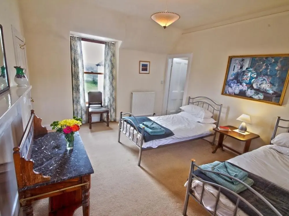 a bedroom with two beds and a table with flowers on it at Biallid House in Newtonmore