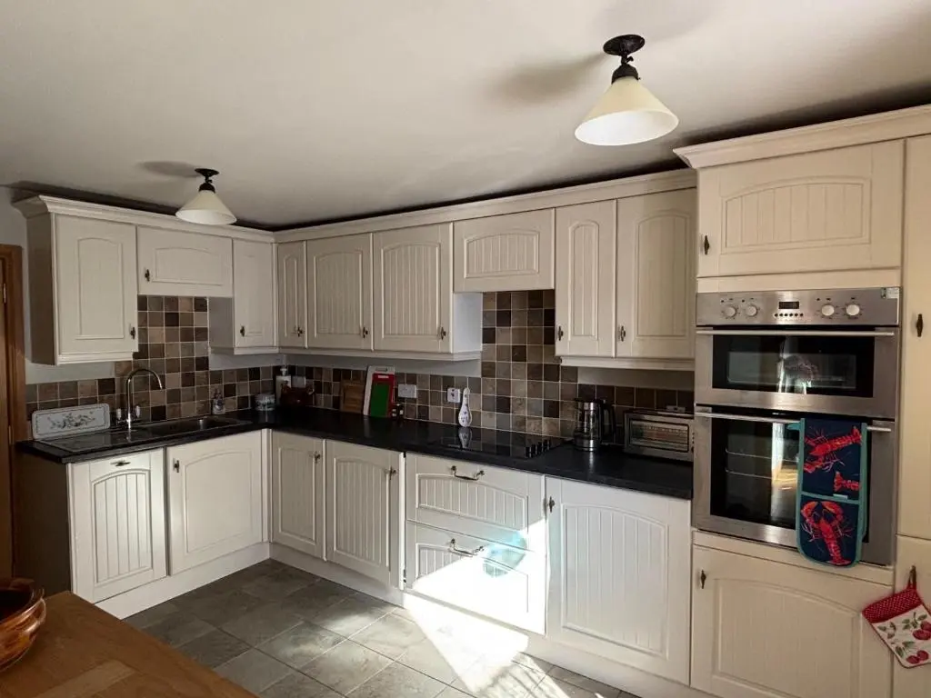 a kitchen with white cabinets and black counter tops at Mary Cottage in Garmouth