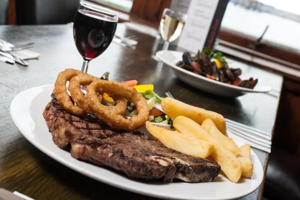 a plate of steak and onion rings and a glass of wine at Tuckers Inn in Invergordon