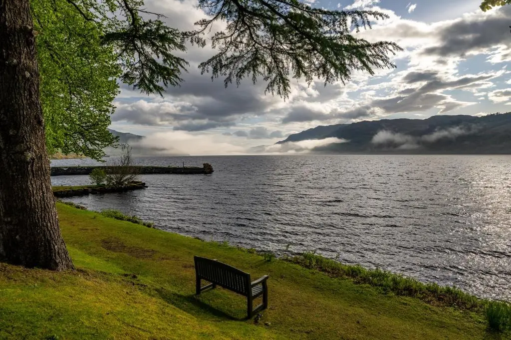 a park bench sitting next to a body of water at The Livingstone Loch Ness OS9 in Fort Augustus