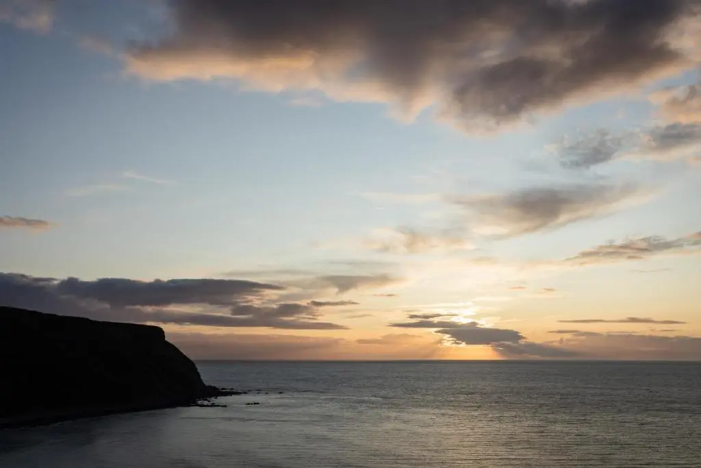 a sunset over the ocean with a cliff at Muckle View in Gardenstown