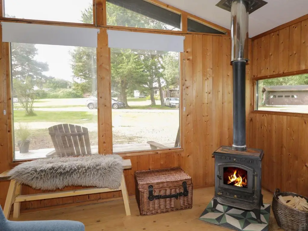 a living room with a wood stove and a chair at Blue Pine Lodge in Dornoch