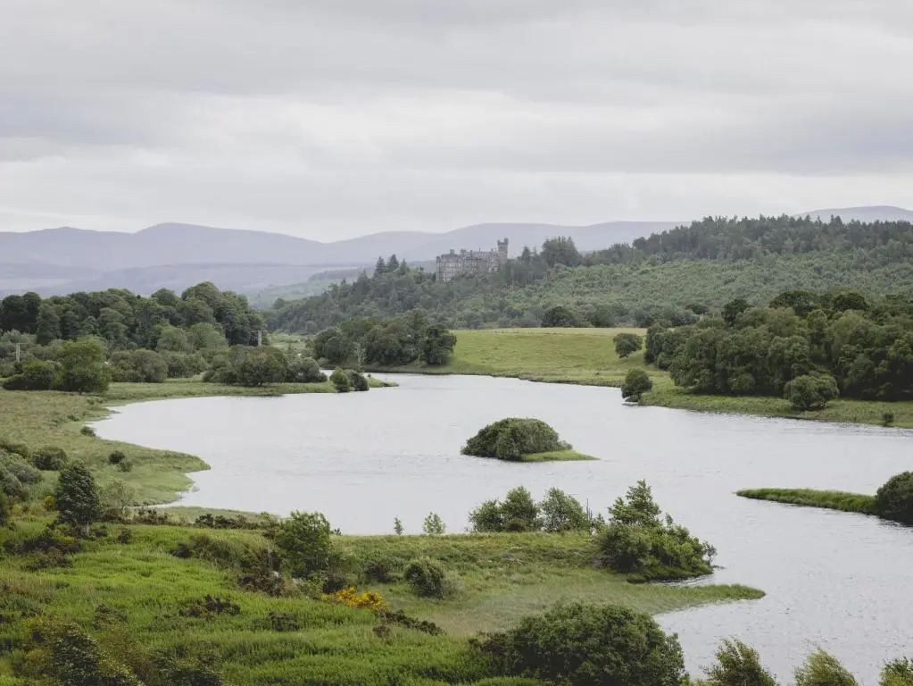 a river in a field with a castle in the distance at Lairg Lodge in Lairg