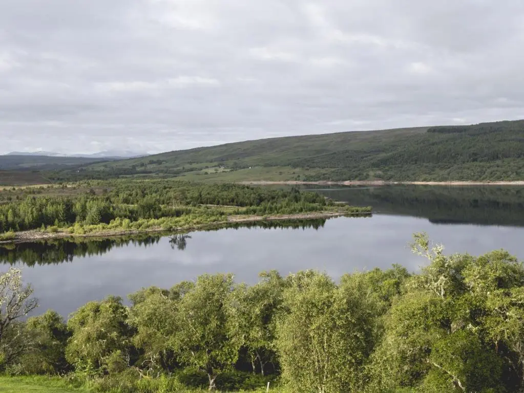 a view of a lake with trees and hills at Lairg Lodge in Lairg