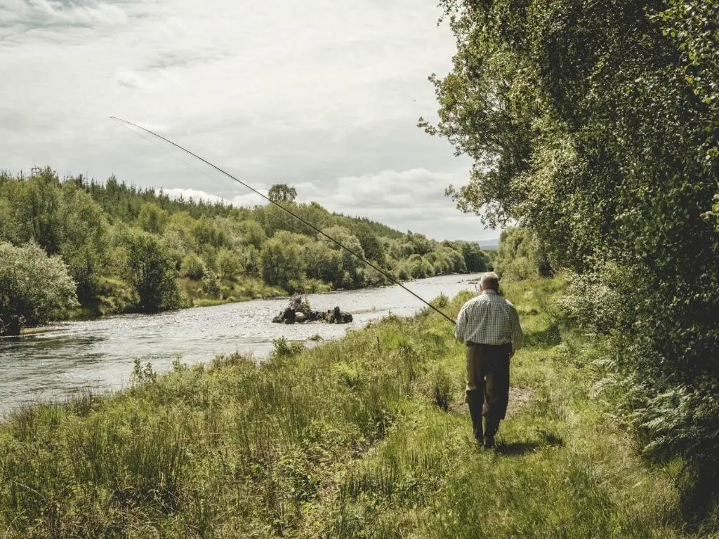 a man is walking along a river while fishing at Lairg Lodge in Lairg