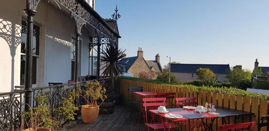 a patio with red chairs and a table on a balcony at The Havelock in Nairn