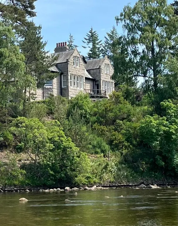 a large house on a hill next to a river at Lys-Na-Greyne Country House in Aboyne