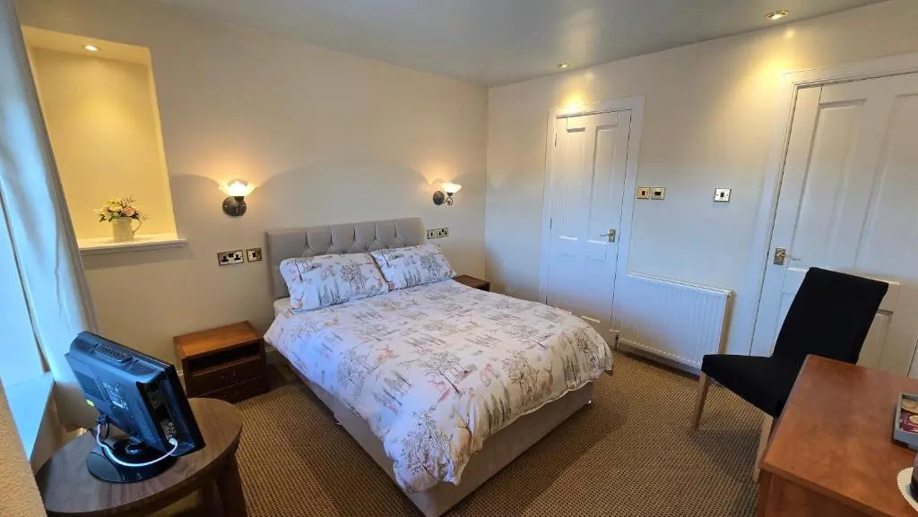 a bedroom with a bed and a table and a tv at The Pitfour Arms Hotel in Mintlaw