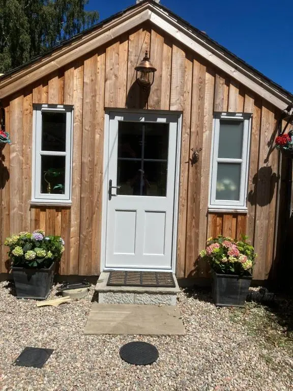 a wooden shed with a white door and two windows at Struan Cottage in Ballater