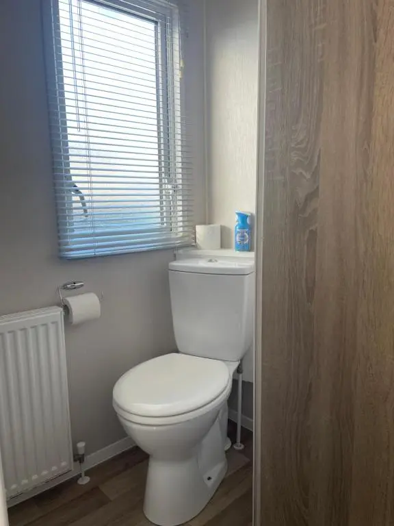 a bathroom with a white toilet and a window at Whispering Dunes - Silver Sands Holiday Park in Lossiemouth
