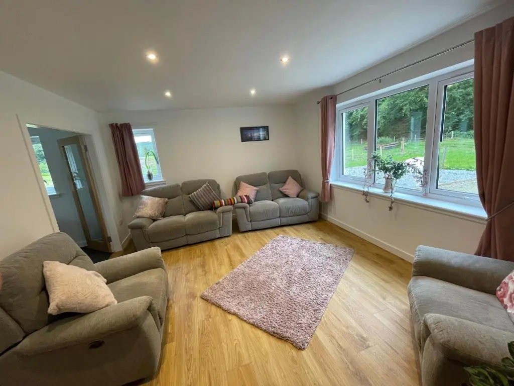 a living room with couches and a large window at Fionnlagh Cottage in Eskadale