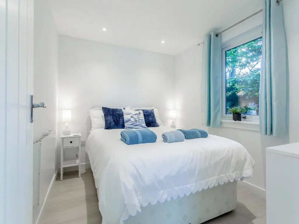 a white bedroom with a large bed with blue pillows at Charlies Cottage in Inverness