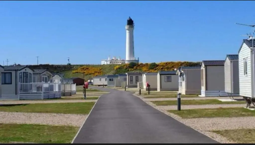 a road with houses and a lighthouse in the background at Spacious Modern Seaside Caravan in Lossiemouth