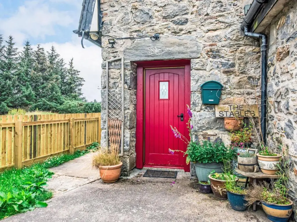 a red door on a stone building with potted plants at Holiday Home Highland Cottage by Interhome in Drumnadrochit