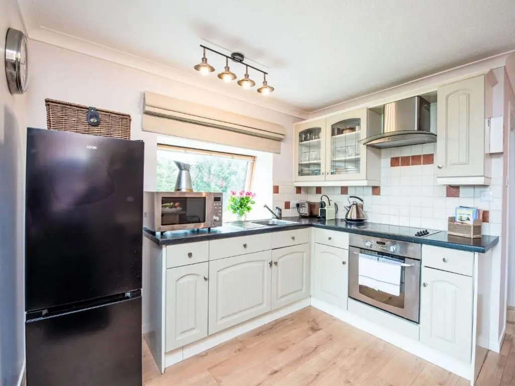 a kitchen with white cabinets and a black refrigerator at Holiday Home Highland Cottage by Interhome in Drumnadrochit