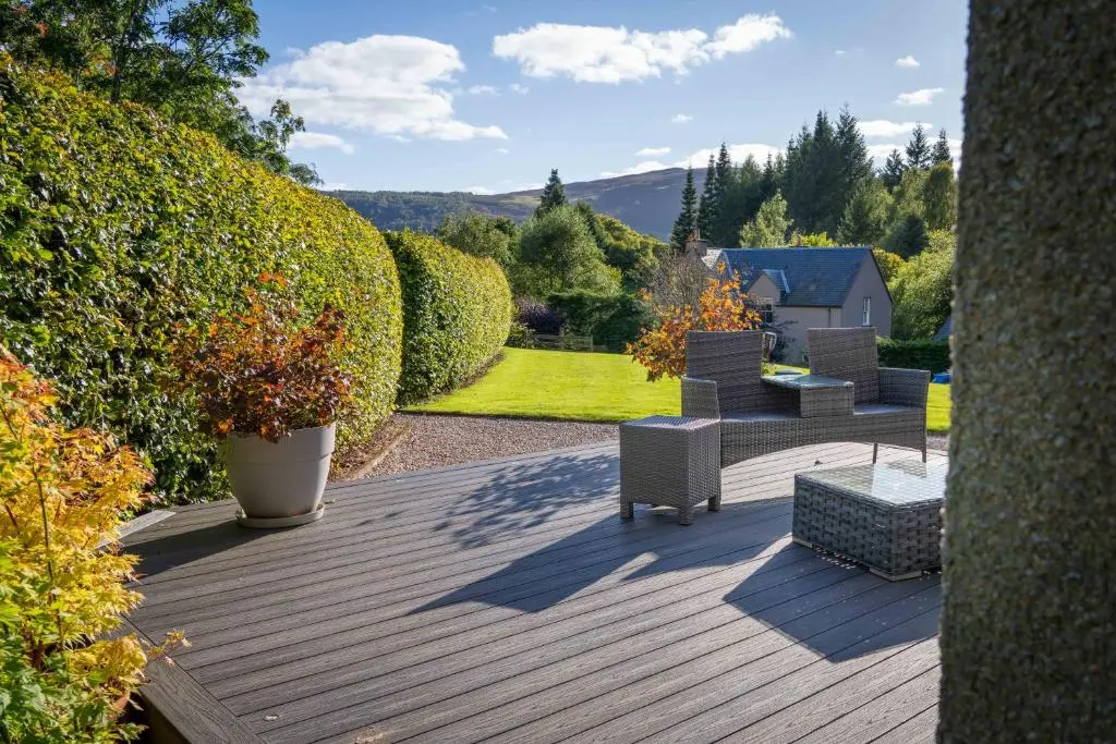 a garden with a wooden deck with chairs and bushes at Glen Tilt House in Bridge of Tilt